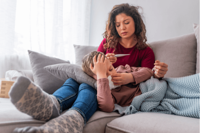 Woman takes temperature of unwell child resting on couch
